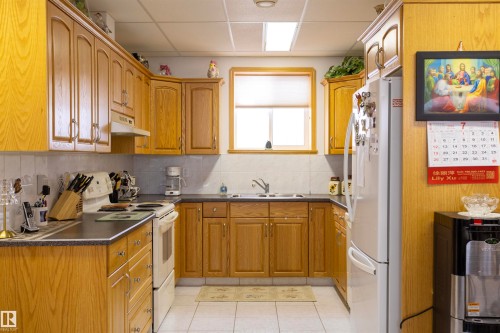 Kitchen featuring oak-finish cabinetry, dark countertops, white tile backsplash, and white tile flooring - 6407 163 Avenue Nw, Edmonton, AB 