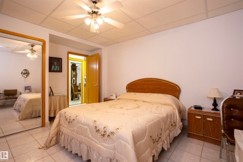 Bedroom featuring tile flooring, a built-in mirrored closet, a ceiling fan with integrated lighting, a solid core door, and a grid panel ceiling - 6407 163 Avenue Nw, Edmonton, AB 