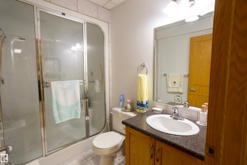 Bathroom featuring a shower enclosure with sliding glass doors, a vanity with wood-finish cabinetry, a dark countertop, an oval undermount sink, and a wall-mounted mirror - 6407 163 Avenue Nw, Edmonton, AB 