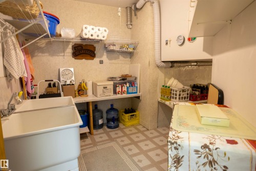 Utility room featuring a double basin utility sink, wall-mounted shelving, and patterned linoleum flooring - 6407 163 Avenue Nw, Edmonton, AB 
