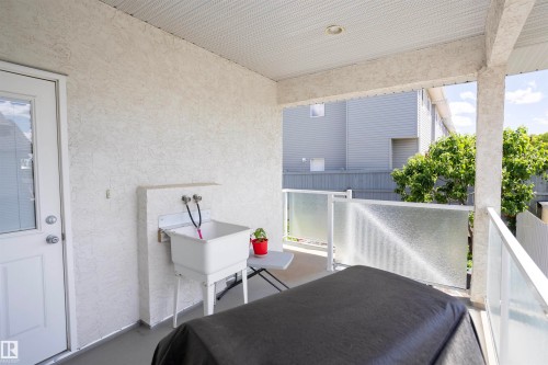 Covered patio area featuring a utility sink with wall-mounted faucets, a white exterior door with a window, and textured exterior walls - 6407 163 Avenue Nw, Edmonton, AB 