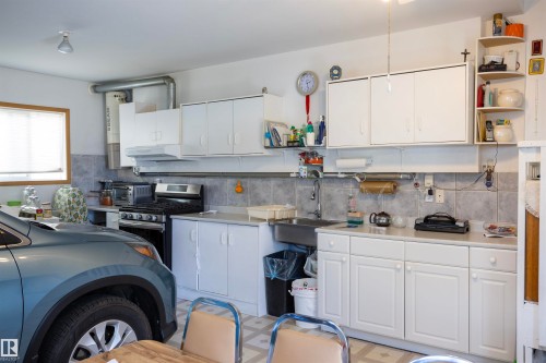 Garage space featuring extensive white cabinetry, a gas range, a stainless steel sink, tile backsplash, and a window for natural light - 6407 163 Avenue Nw, Edmonton, AB 