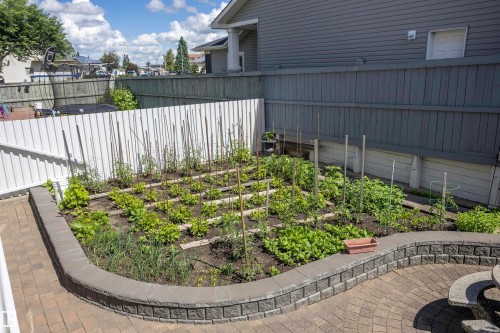 Paver patio with a curved stone retaining wall surrounding a garden bed - 6407 163 Avenue Nw, Edmonton, AB 