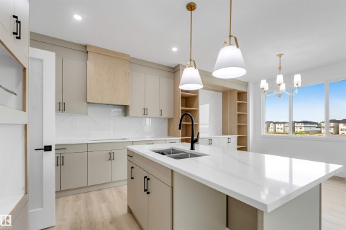 Open concept kitchen featuring an expansive island with an undermount double sink and matte black faucet, light wood-finish flooring, recessed lighting, and a window framing a residential area - 4234 63 Street, Beaumont, AB - Indoor Photo Showing Kitchen With Double Sink