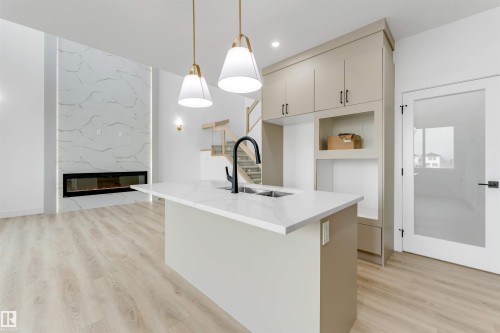 Open-concept space featuring a kitchen island with integrated sink, white quartz countertops, and matte black faucet - 4234 63 Street, Beaumont, AB - Indoor Photo Showing Kitchen With Fireplace