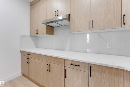 Modern kitchen featuring light wood-finish cabinetry with black hardware, white countertops, a matching full-height white backsplash, and a stainless steel range hood - 4234 63 Street, Beaumont, AB - Indoor Photo Showing Kitchen