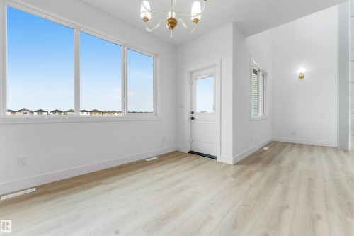 Open-concept living space featuring expansive windows, light wood-finish flooring, and a white paneled exterior door - 4234 63 Street, Beaumont, AB - Indoor Photo Showing Other Room