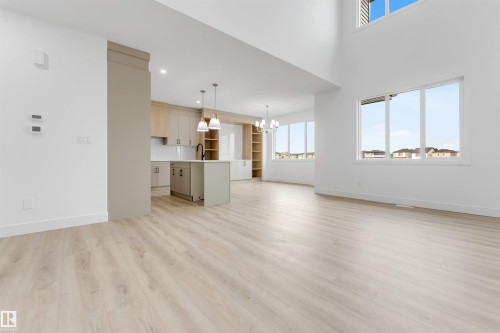 Spacious open-concept living area featuring light wood-finish flooring, high ceilings, and large windows - 4234 63 Street, Beaumont, AB - Indoor