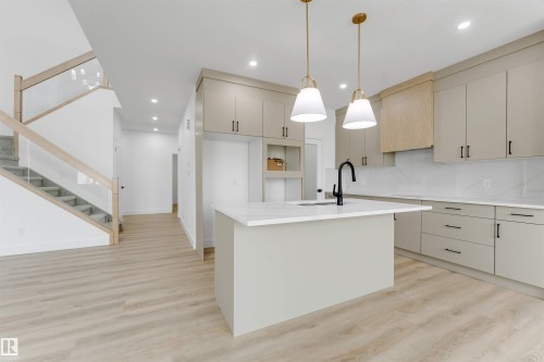 Modern kitchen featuring light cabinetry, a central island with a sink, white countertops, and contemporary pendant lighting - 4234 63 Street, Beaumont, AB - Indoor Photo Showing Kitchen With Upgraded Kitchen