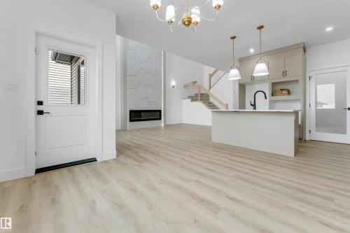 Open-concept living area with light wood-finish flooring, a contemporary fireplace feature wall, and a kitchen island with pendant lighting - 4234 63 Street, Beaumont, AB - Indoor Photo Showing Kitchen