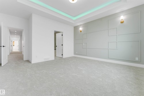 Spacious room featuring tray ceiling with accent lighting, textured wall paneling, two gold-toned wall sconces, and light grey carpeting - 4234 63 Street, Beaumont, AB - Indoor Photo Showing Other Room