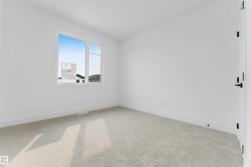 Bright interior room featuring a large window, light-toned carpeting, white baseboards, and a white door with black hardware - 4234 63 Street, Beaumont, AB - Indoor Photo Showing Other Room