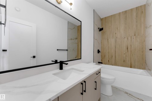 Bathroom featuring a floating vanity with a single basin, a large wall-mounted mirror, a tub-shower combination with wood-look and marble-look tiling, matte black fixtures, and marble-look floor tiling - 4234 63 Street, Beaumont, AB - Indoor Photo Showing Bathroom