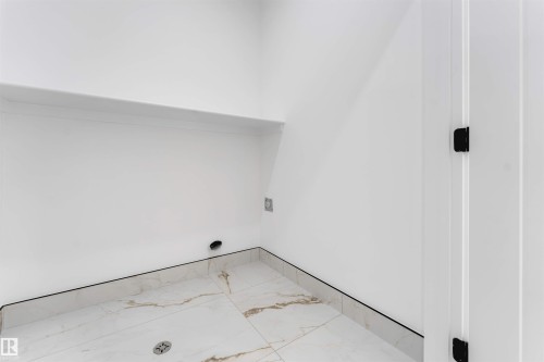White interior space featuring a built-in shelf, marble-look tile flooring, and a white door with black hardware - 4234 63 Street, Beaumont, AB - Indoor Photo Showing Other Room