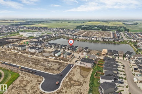 Aerial perspective of a developing residential community featuring a prominent central pond, new road construction, and surrounding green fields - 4234 63 Street, Beaumont, AB - Outdoor With View