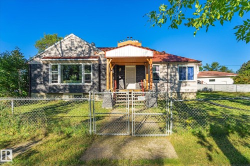 Chain-link perimeter fencing with double gates, a covered porch with wooden posts, and a gabled roofline - 11008 109 Street Nw, Edmonton, AB 