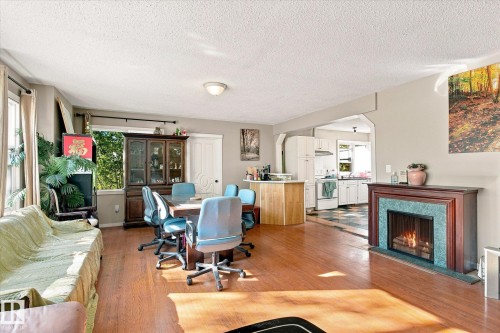 Wood-finish flooring throughout the main living space, a decorative fireplace with a tile surround, and an architectural archway leading to the kitchen - 11008 109 Street Nw, Edmonton, AB 