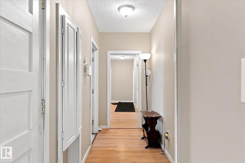 Bright hallway featuring warm wood-finish flooring, white six-panel doors with polished hardware, soft neutral wall finishes, and recessed ceiling lighting throughout - 11008 109 Street Nw, Edmonton, AB 