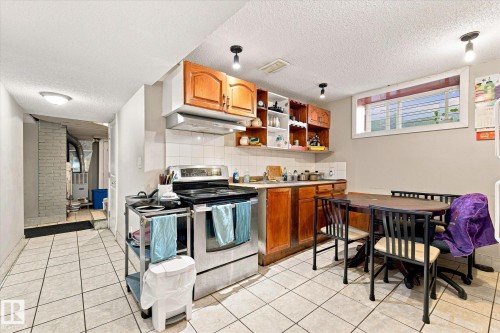 Kitchen featuring wood-finish cabinetry, white tile flooring, a built-in range, and a window with white trim - 11008 109 Street Nw, Edmonton, AB 