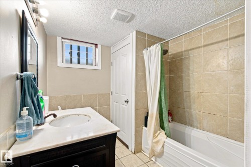 Vanity with a white countertop and basin sink, wall-mounted mirror, white bathtub, and tile shower surround - 11008 109 Street Nw, Edmonton, AB 