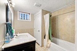 Vanity with a white countertop and basin sink, wall-mounted mirror, white bathtub, and tile shower surround - 