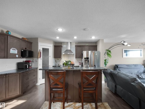 Kitchen featuring dark wood-finish cabinetry, stainless steel appliances, dark stone-finish countertops, and a central island with bar seating - 1216 29 Avenue Nw, Edmonton, AB - Indoor Photo Showing Kitchen With Stainless Steel Kitchen