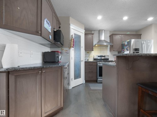 Kitchen featuring wood-finish cabinetry, granite countertops, tile backsplash, stainless steel appliances, and wood-finish flooring - 1216 29 Avenue Nw, Edmonton, AB - Indoor Photo Showing Kitchen