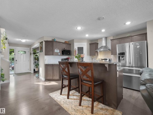 Kitchen featuring wood-finish flooring, recessed lighting, a built-in stainless steel range hood, stainless steel refrigerator, and a kitchen island with a stone-finish countertop - 1216 29 Avenue Nw, Edmonton, AB - Indoor Photo Showing Kitchen With Stainless Steel Kitchen With Upgraded Kitchen
