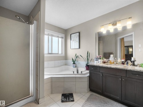 Bathroom featuring a corner soaking tub with tile surround, a shower enclosure with glass door, a dark wood-finish vanity with a light-toned countertop, and a wall-mounted light fixture above a mirror - 1216 29 Avenue Nw, Edmonton, AB - Indoor Photo Showing Bathroom