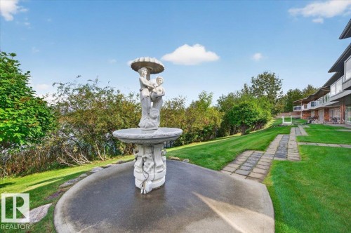 Sculptural fountain centerpiece with a circular paved base, manicured lawn, and paved pathway - #7 10500 103 Av, Morinville, AB 