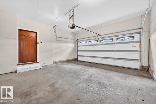 Attached two-car garage featuring a concrete floor, automatic garage door opener, and a wooden entry door with decorative detailing - #7 10500 103 Av, Morinville, AB 