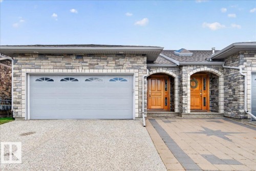 Stone veneer exterior with arched entryways, two light wood-finish entry doors, a two-car garage with transom windows, and a paver driveway - #7 10500 103 Av, Morinville, AB 