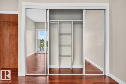 Mirrored sliding closet doors, built-in shelving, rich wood-finish flooring, and a decorative wood door - #7 10500 103 Av, Morinville, AB 
