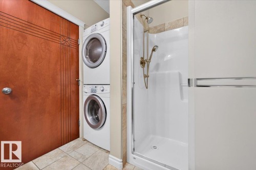 Stackable washer and dryer, shower enclosure with sliding glass door, white shower base, and tiled shower surround - #7 10500 103 Av, Morinville, AB 
