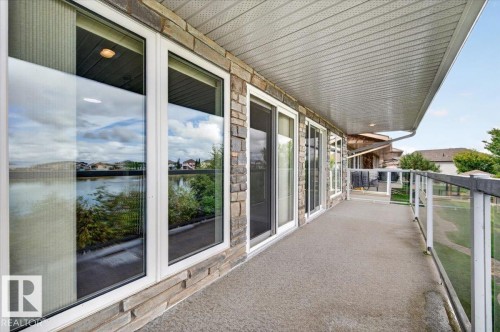 Expansive balcony with a concrete surface, stone facade, multiple sliding glass doors, and a glass-paneled railing - #7 10500 103 Av, Morinville, AB 