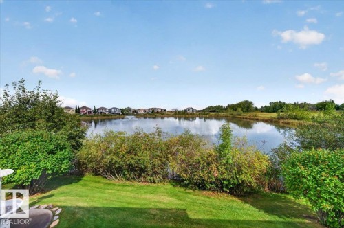 Expansive backyard featuring a manicured lawn, mature shrubs, and a prominent pond - #7 10500 103 Av, Morinville, AB 