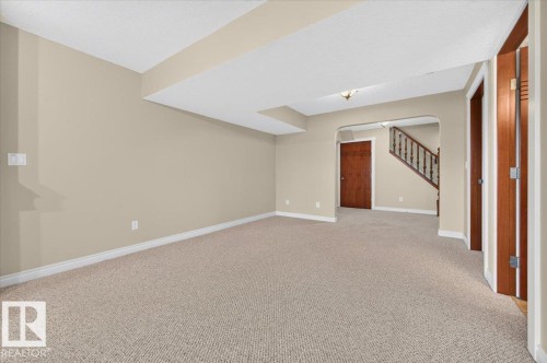 Carpeted flooring throughout, neutral wall color, staircase with wooden banister, and wood-finish interior doors - #7 10500 103 Av, Morinville, AB 