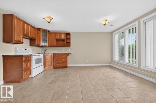 Tile flooring, integrated kitchen cabinetry, white range, built-in sink, and large windows - #7 10500 103 Av, Morinville, AB 