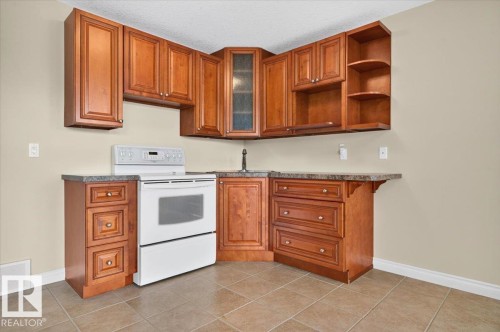Kitchenette featuring wood-finish cabinetry, tile flooring, built-in electric range, and a corner sink - #7 10500 103 Av, Morinville, AB 