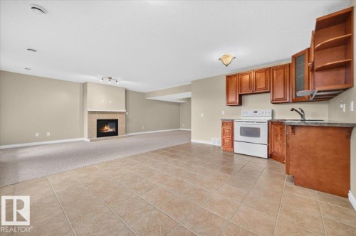 Recessed lighting, tiled flooring, wood cabinetry with glass accents, white range, and a fireplace with a stone surround - #7 10500 103 Av, Morinville, AB 