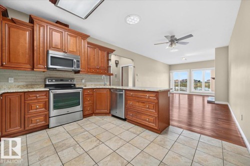 Kitchen with wood cabinetry, stainless steel appliances, tile flooring, and a stone countertop - #7 10500 103 Av, Morinville, AB 
