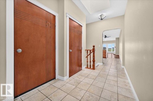 Tiled flooring, two wood-finish doors with decorative detailing, wood-finish staircase railing, arched entryway, and a semi-flush mount ceiling fixture - #7 10500 103 Av, Morinville, AB 