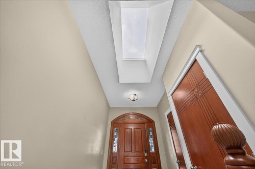 Skylight with a textured ceiling, double-panel wood door with decorative glass, and a wall-mounted light fixture - #7 10500 103 Av, Morinville, AB 