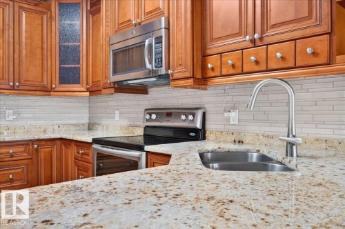 Kitchen featuring light wood-finish cabinetry, speckled countertops, stainless steel appliances, and a tiled backsplash - #7 10500 103 Av, Morinville, AB 