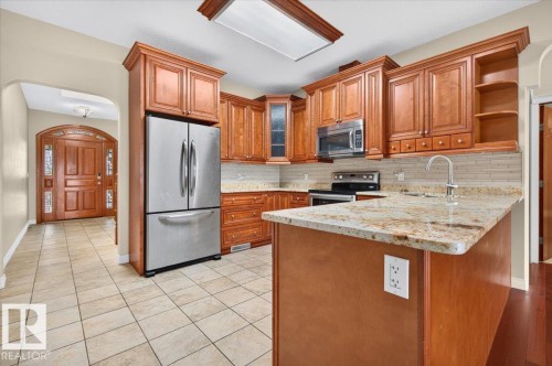 Kitchen featuring wood cabinetry, stainless steel appliances, a tiled backsplash, and stone countertops - #7 10500 103 Av, Morinville, AB 