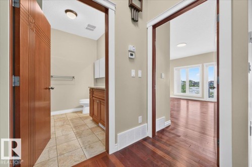 Warm wood-finish flooring extends through an open doorway, complementing the light-colored walls and white trim - #7 10500 103 Av, Morinville, AB 
