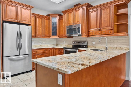 Kitchen with wood-finish cabinetry, stainless steel appliances, and a mosaic tile backsplash - #7 10500 103 Av, Morinville, AB 