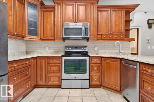 Wood-finish cabinetry with glass accents, stainless steel appliances, granite countertops, tile backsplash, and tile flooring - #7 10500 103 Av, Morinville, AB 