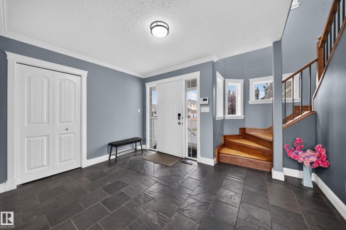Slate tile flooring, white trim, wood staircase with black metal spindles, built-in closet, and a front entry door with sidelights - 6904 18 Avenue Sw, Edmonton, AB 