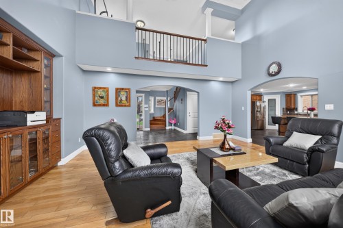 High ceilings with architectural elements, wood-finish flooring, built-in wood cabinetry with glass fronts, archways, and an upper-level railing - 6904 18 Avenue Sw, Edmonton, AB 